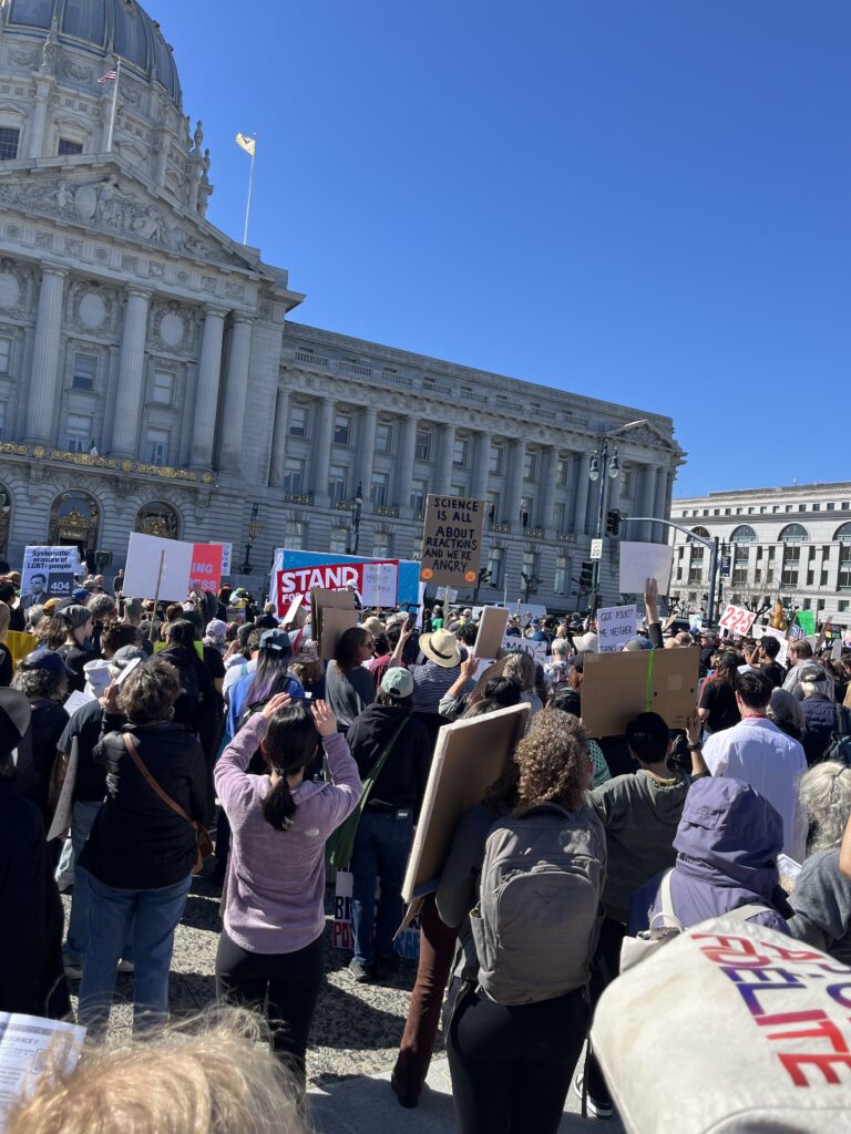 A group of rally-goers stands in front of San Francisco City Hall, holding signs in support of science.
