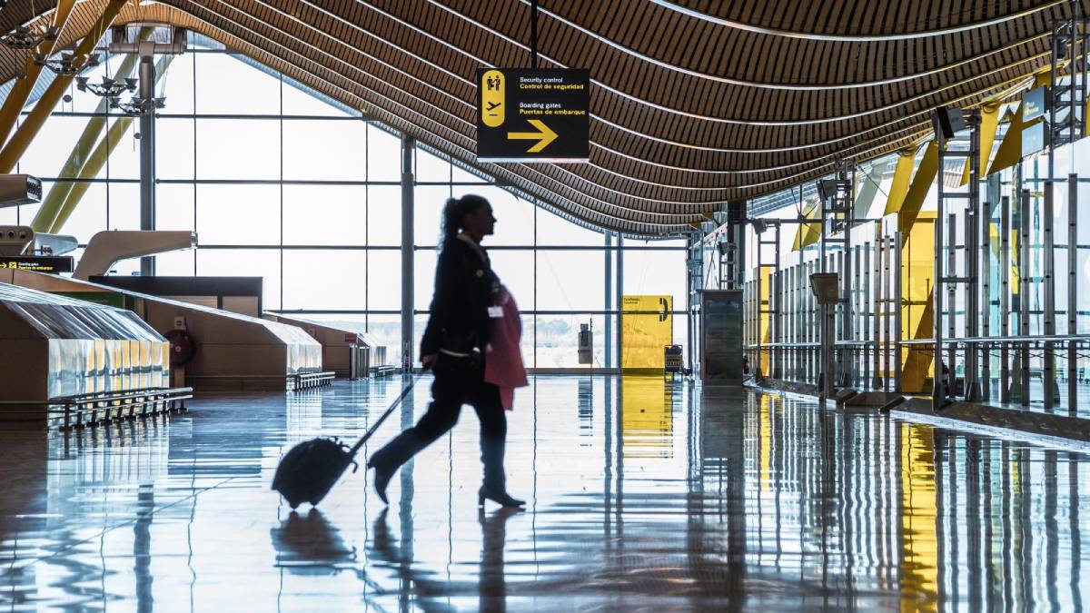A woman walks through an empty airport terminal with a small rolling suitcase.
