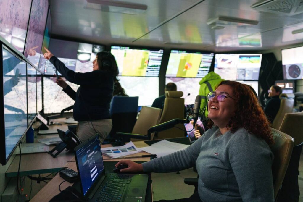 People surrounded by computer monitors in a darkened room