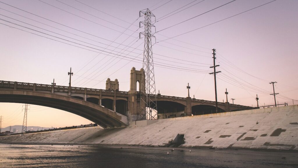 The Los Angeles River passes under a bridge at sunset.