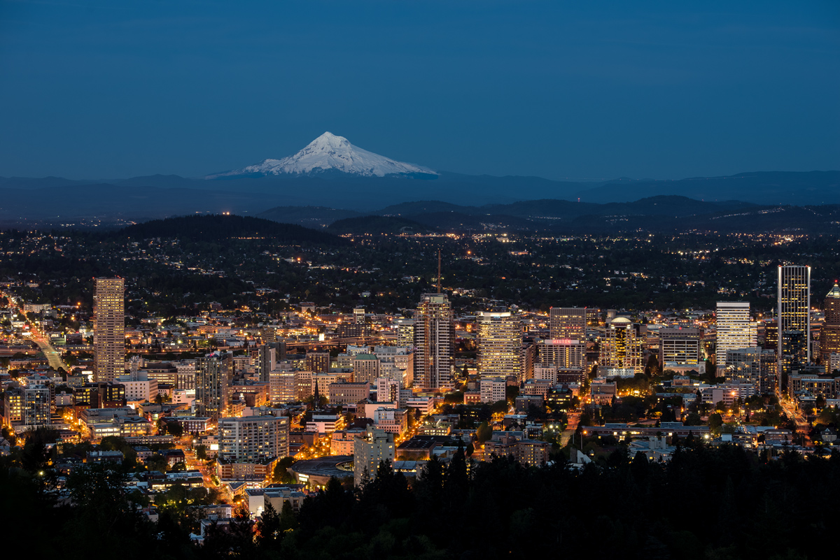 El Monte Hood cubierto de nieve se alza a lo lejos, más allá del horizonte nocturno de Portland, Oregón.