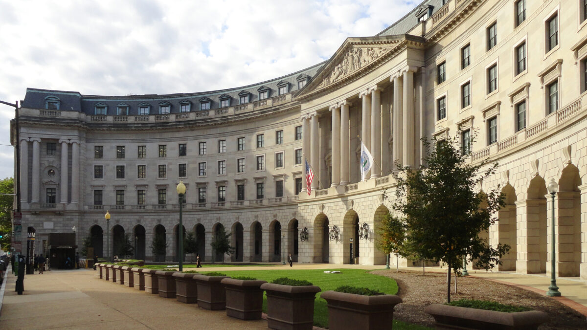 A curved building with classic pillars is seen from the sidewalk.