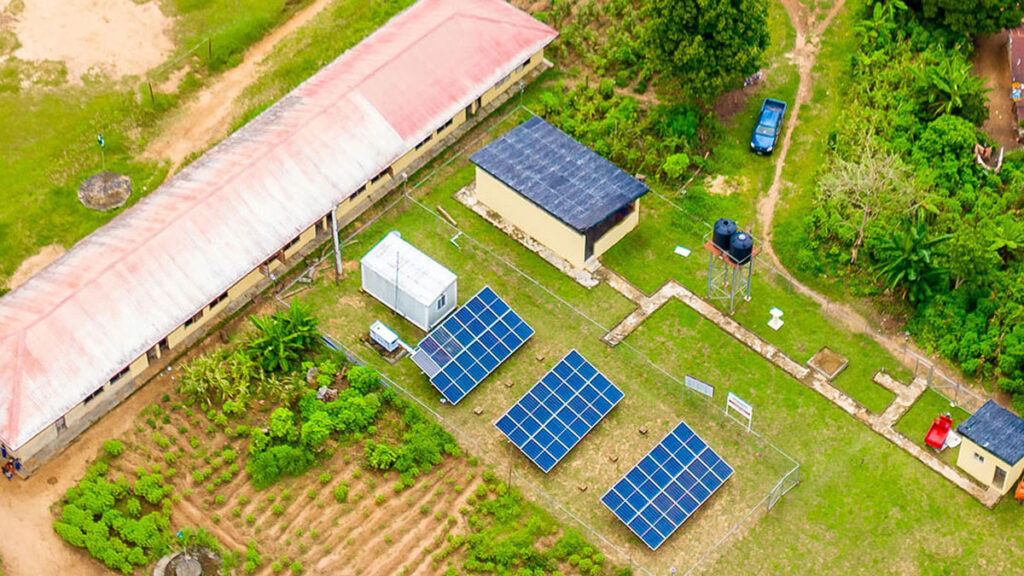 An aerial shot shows some buildings and solar panels against a lush green landscape.