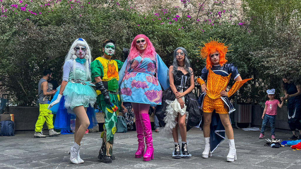 Cinco personas posan para la cámara con mucho maquillaje y vestuarios coloridos.