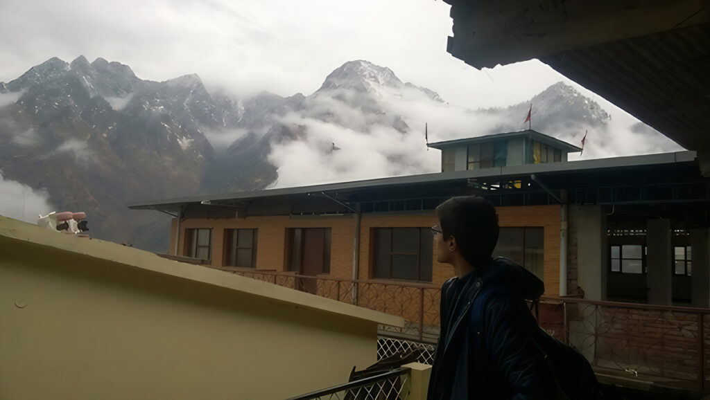 A person looks over the roofs of buildings toward mountains shrouded in clouds.
