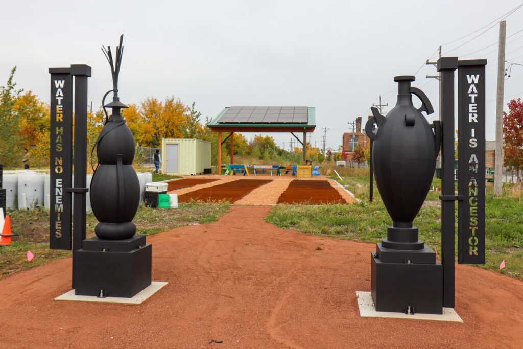 Two large sculptures resembling water jugs mark a pathway to a park.