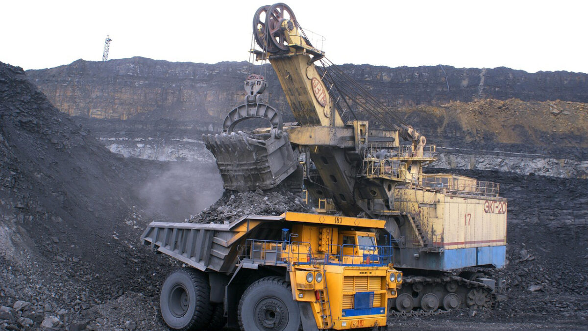 A large vehicle dumps a load of coal into another large vehicle.