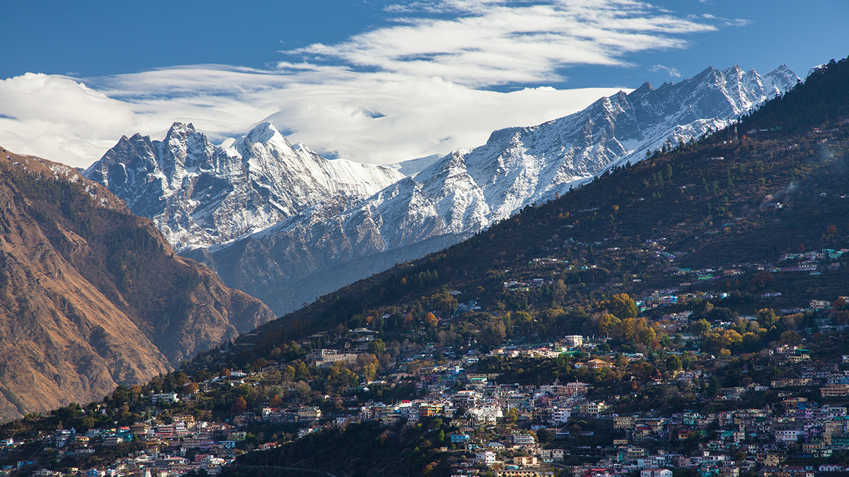 Wide view of a mountainside city in the foreground with snow-capped mountains in the background