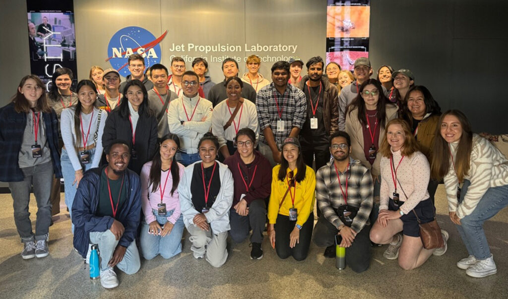 About 30 students pose for a photo in front of signage for NASA’s Jet Propulsion Laboratory.