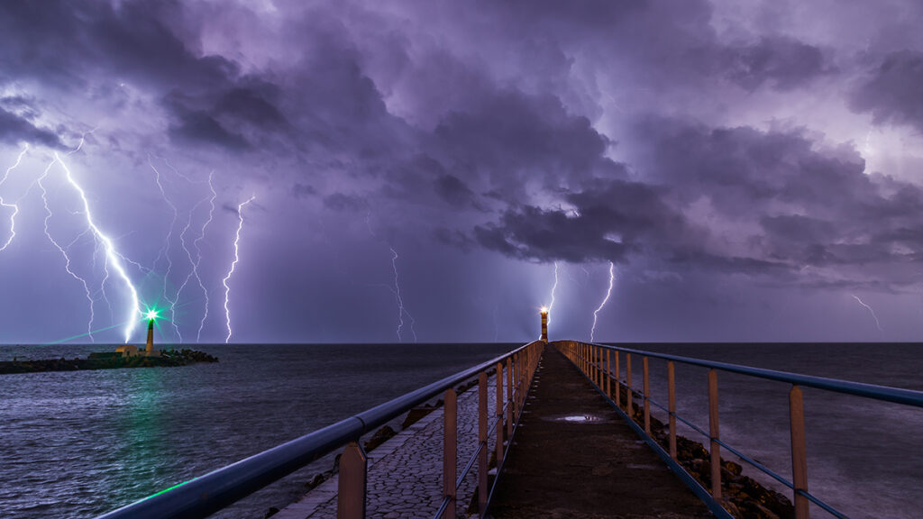 Lightning strikes the ocean behind two lighthouses.