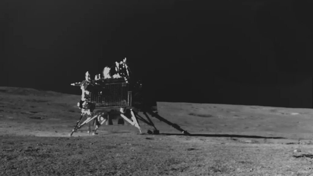 A boxy machine with legs at its corners sits atop a battered gray landscape.