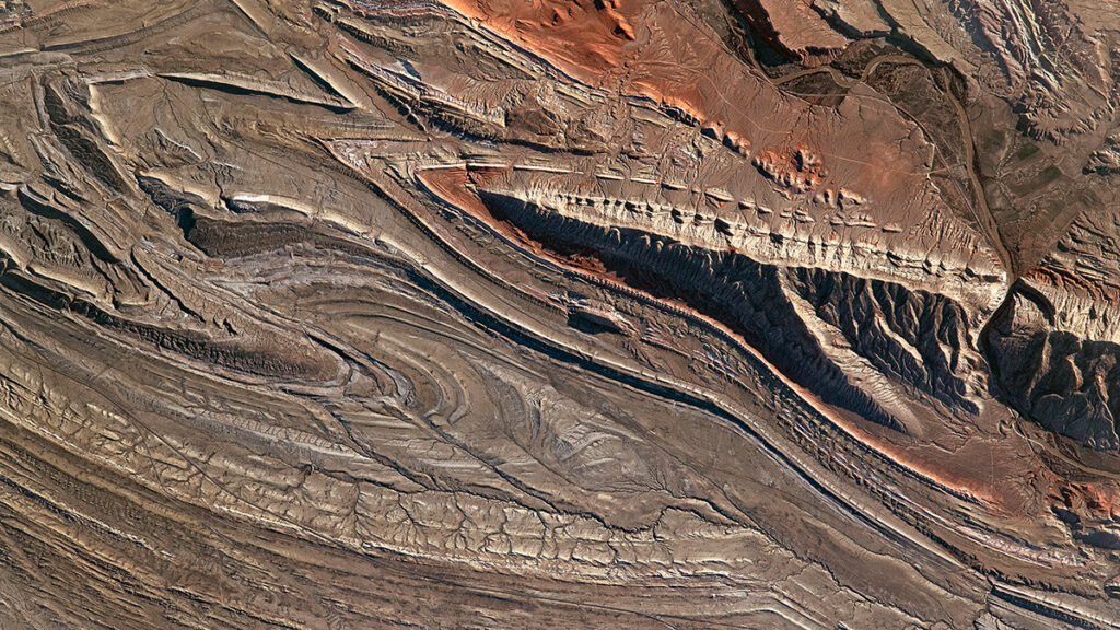 Satellite image of a brown and red rocky landscape with striking geologic folds and curves