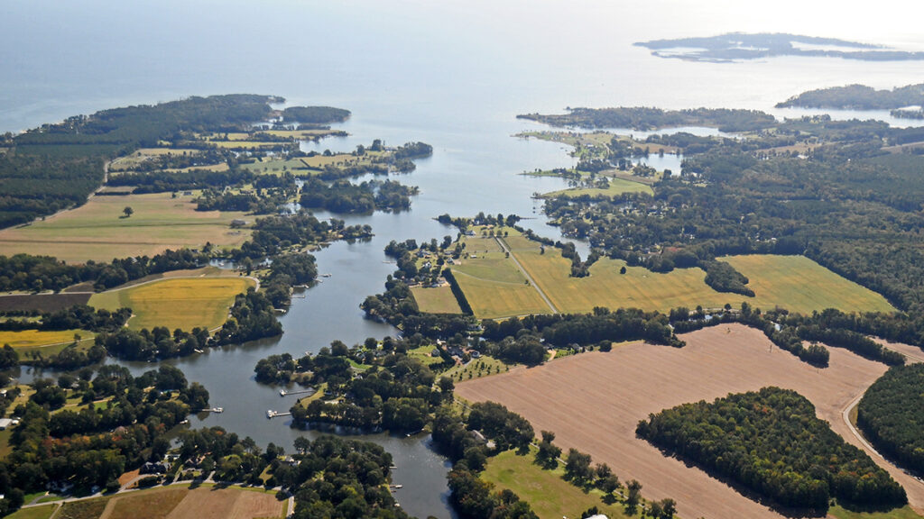 Chesapeake Bay, with its tree-lined waterfronts curving along the river toward the ocean, is pictured from above.