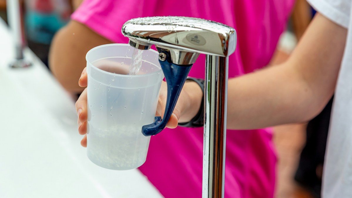 A person fills a plastic cup with water from a faucet.