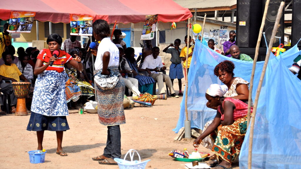 A group of people in the foreground with blue malaria prevention nets.