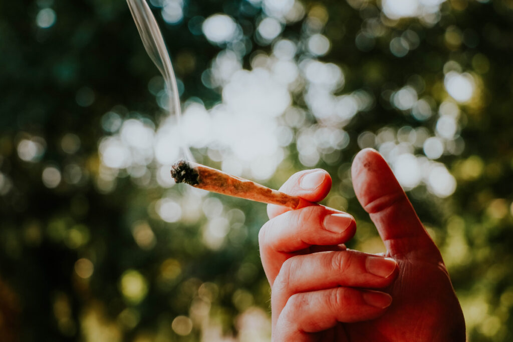A hand holding a smoking marijuana joint