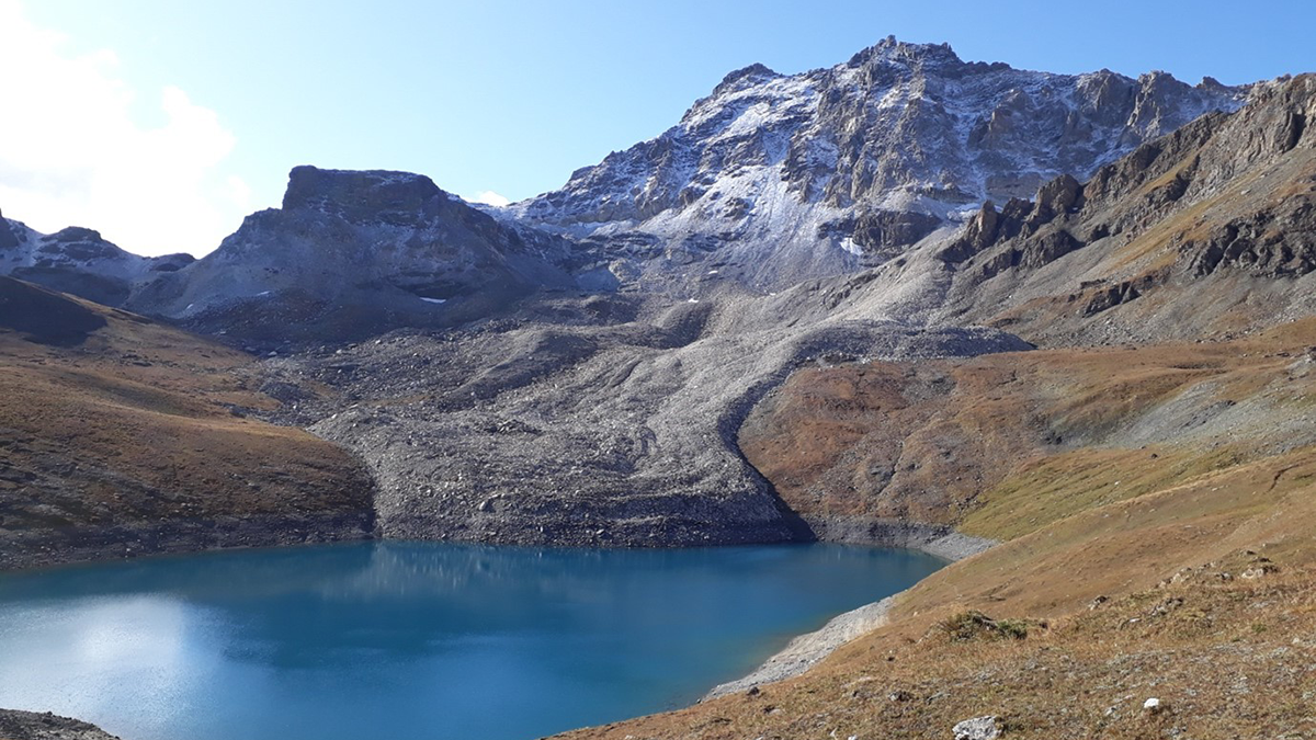 Photo of a mountainous region with a rock glacier and pool of water in front.