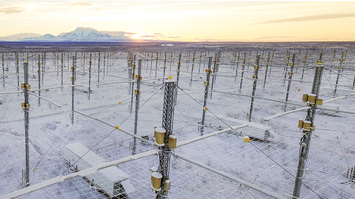 A network of antenna sticks up from a snowy landscape and connected by mesh wires stretch far off into the distance. Snowy mountains are on the horizon.