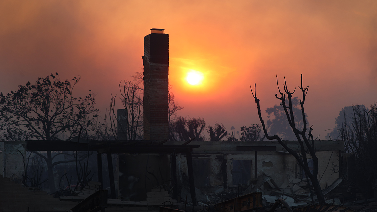 A burned-down house has only a frame and a chimney remaining. A few burned trees surround the house, and the Sun is rising or setting in a smoky red sky.