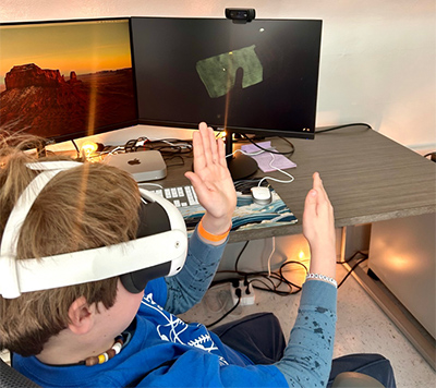 A middle school student wearing a virtual reality headset holds his hands in front of his face while interacting virtually with a coral core.