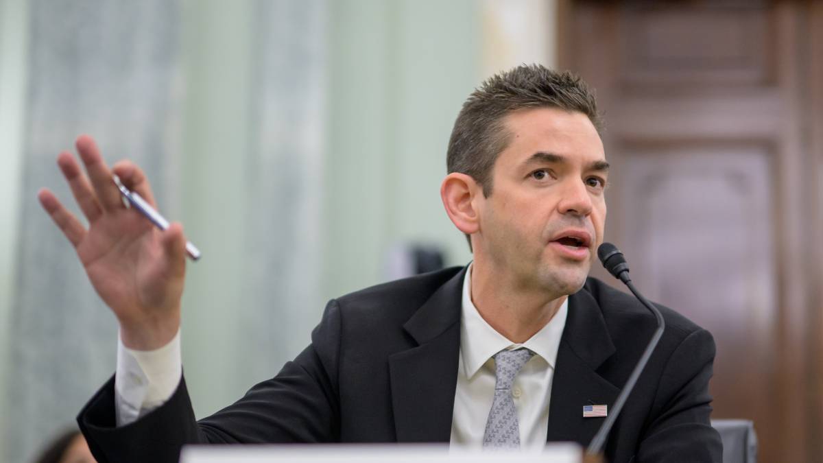 Jared Isaacman, in a suit with an American flag pin, sits at a desk in a Senate committee room