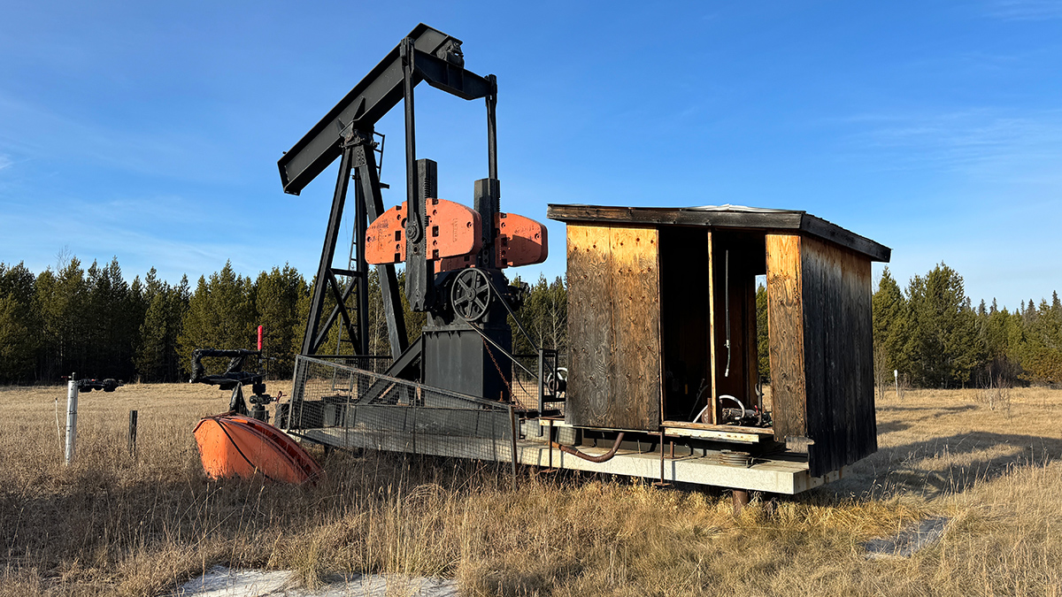 An old oil pump in a field of yellow grass with trees in the background