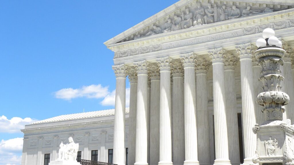 The U.S. Supreme Court Building, a white stone building with large pillars, under a blue sky.