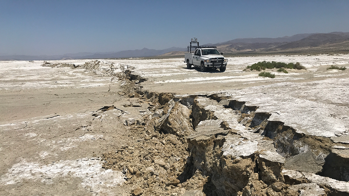 A cracked and deformed rupture in the Earth's surface with a truck in the background.