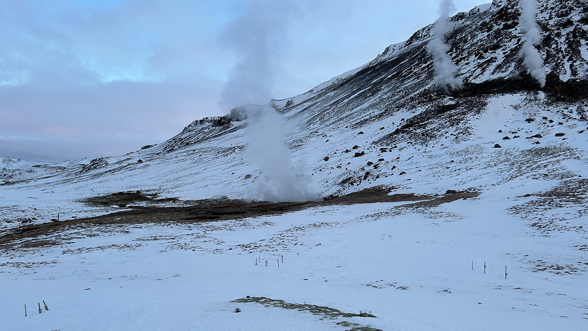 Snow-covered surface with dark patches of soil uncovered. Steam is rising from some patches.
