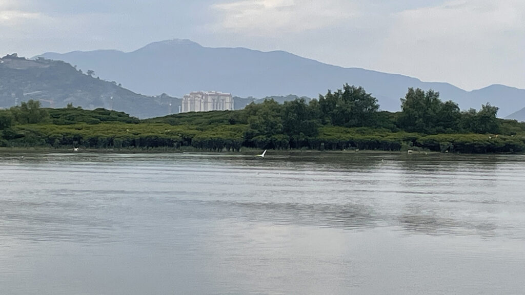 一条河流及后面可见的绿色河岸，山峦和一处灰色的建筑。