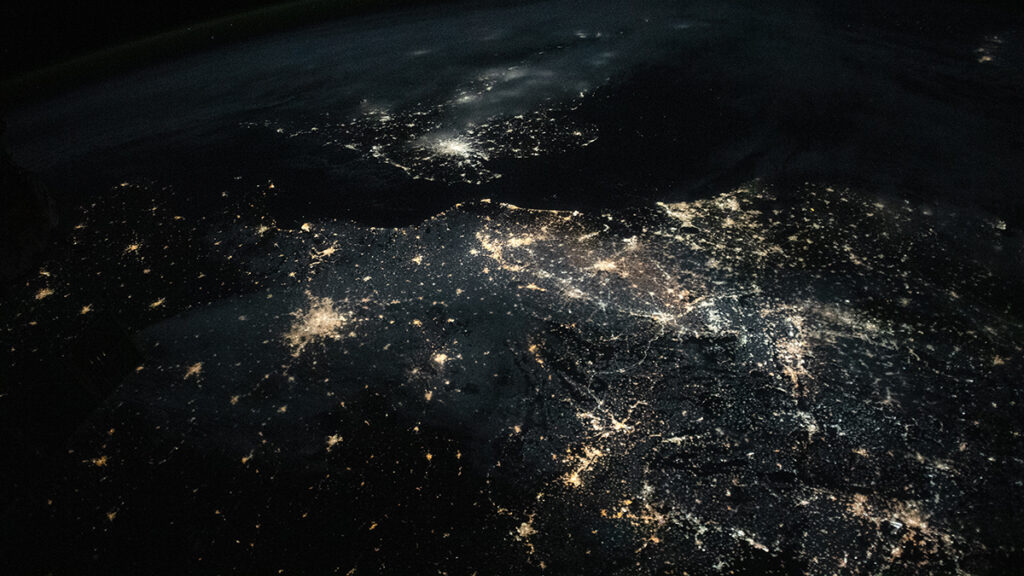 A satellite image of northwestern Europe at night shows several urban centers that appear as bright clusters of light.