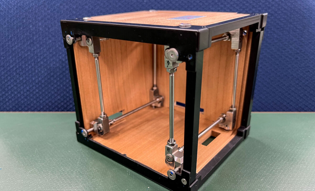 A wooden cube, framed with black metal, rests on a table against a blue background.