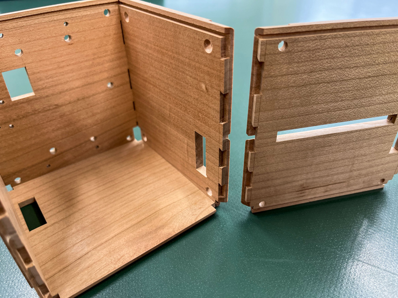 Three sides of a cube are shown assembled, with a fourth side beside it, showing cuts into the wood that join the wood together.