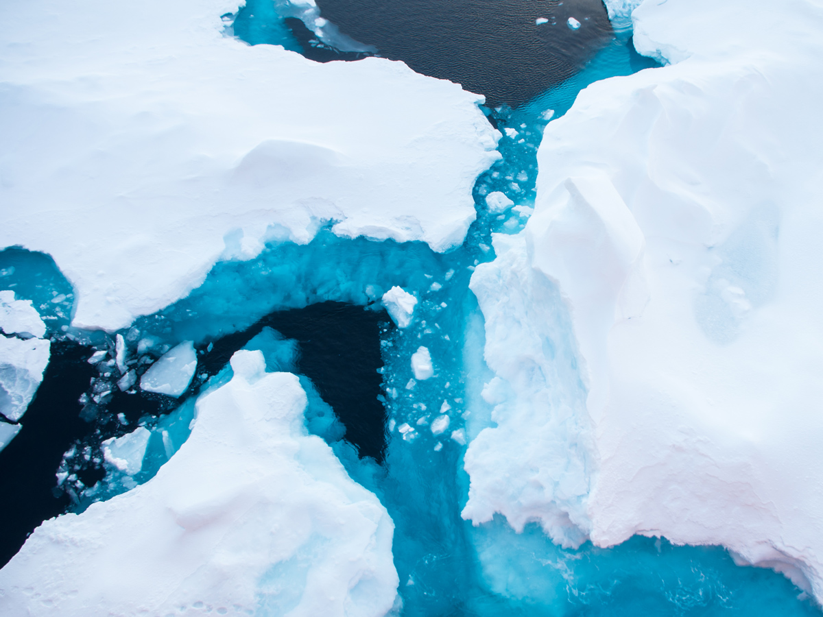 White floating sea ice has jagged edges where it meets the dark and light blue ocean waters.