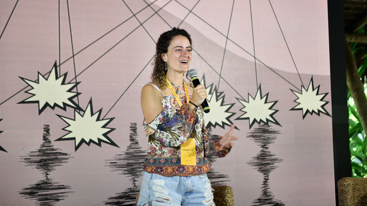 A person speaks into a microphone in front of a background display with cartoon explosions and seismic squiggles.