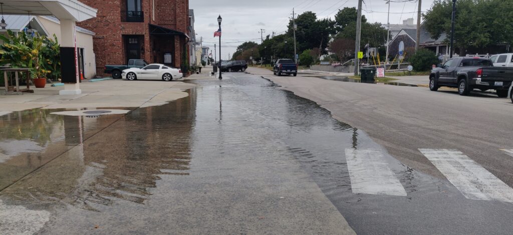 A town street with cars. One side of the street is covered in water. 