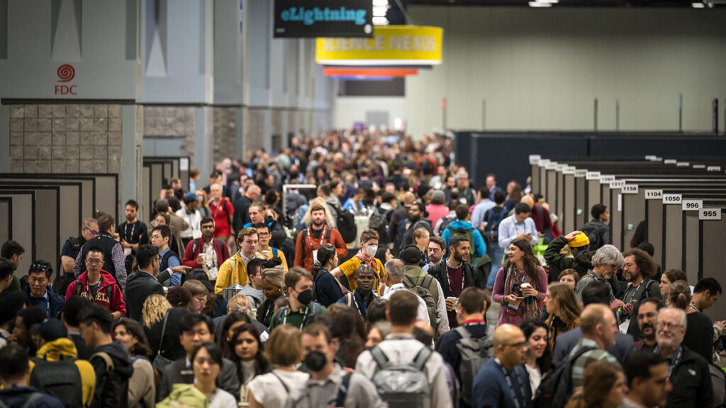 A crowd of people walk in a corridor between rows of posters at a scientific conference.
