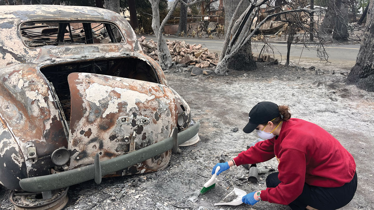 A researcher collects a sample of dust near a structure burned in the Eaton Fire.
