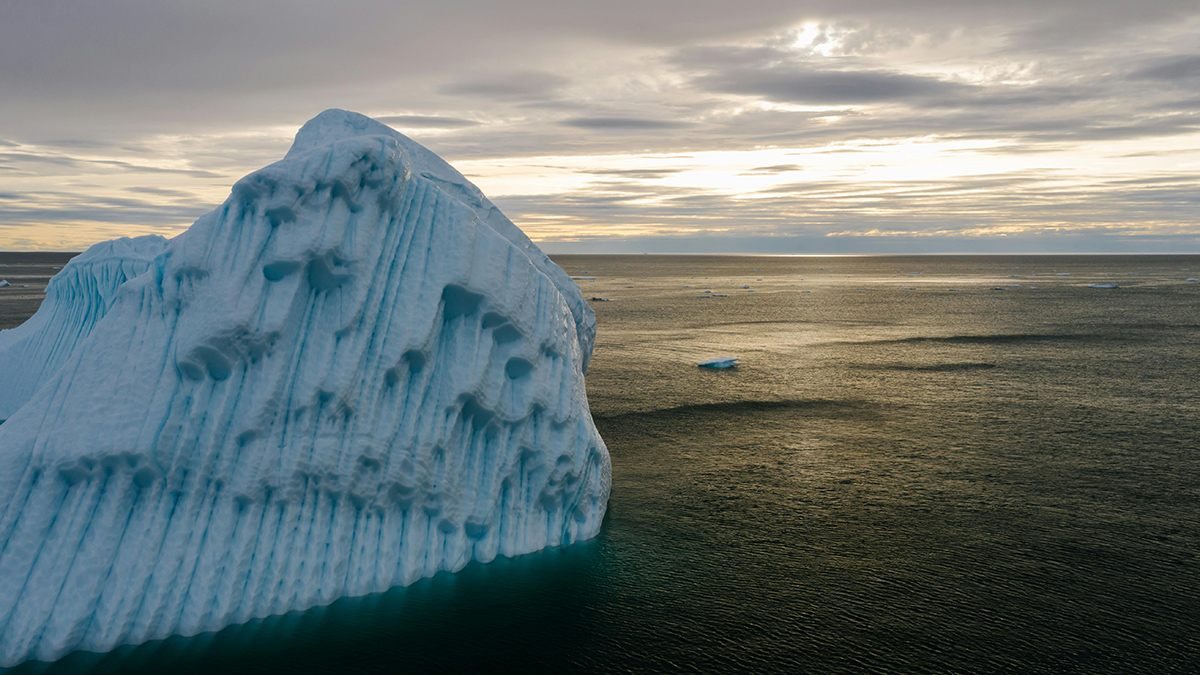 A large iceberg floats in blue Arctic Ocean water.