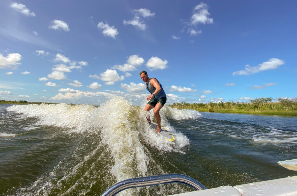 A man in a life vest surfs behind a powerboat.