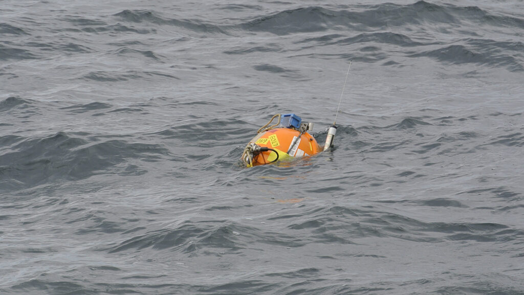 An orange, soccer ball–sized sphere with electronic equipment attached to it floats in the ocean.