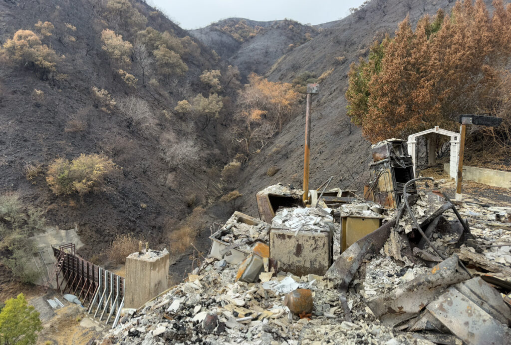 The burned wreckage of a house against the backdrop of a mostly burned mountain. Only a few items, including a white gazebo, are recognizable.