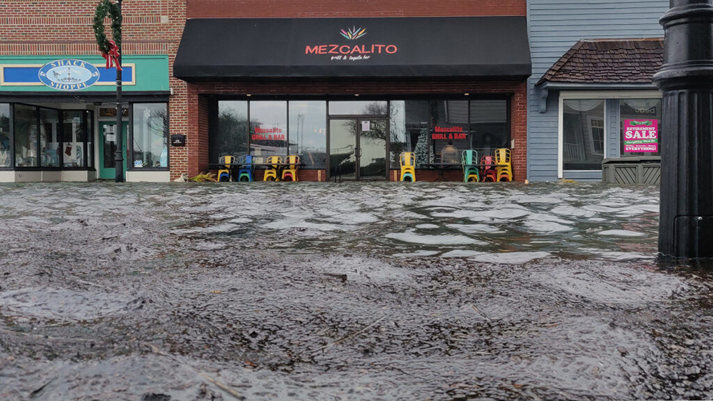 Floodwaters rise above the street and sidewalk in a downtown area.
