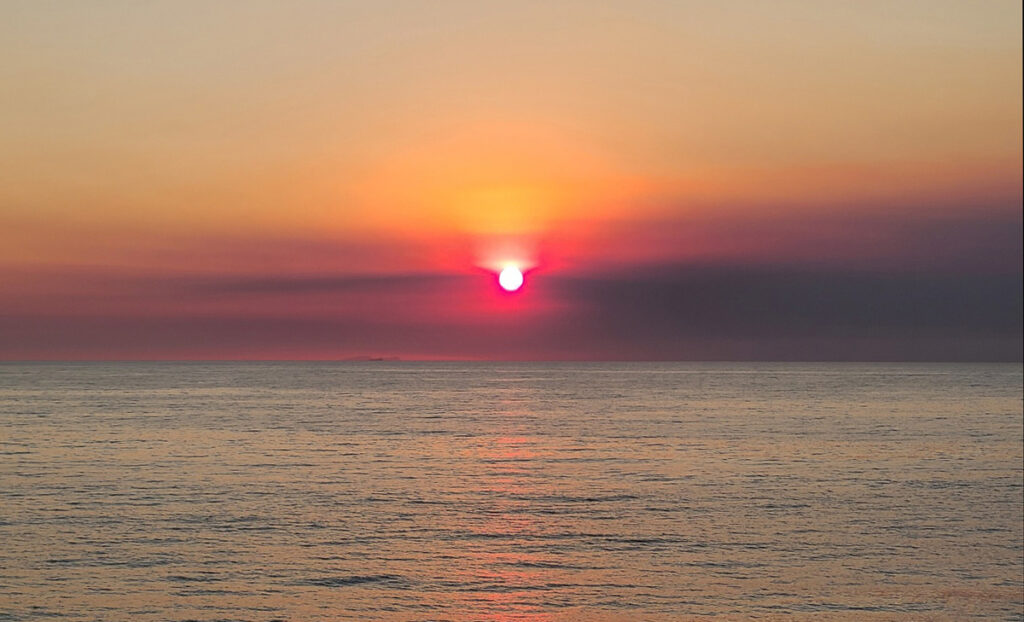 Dark bands of ash obscure a sunset over the ocean.