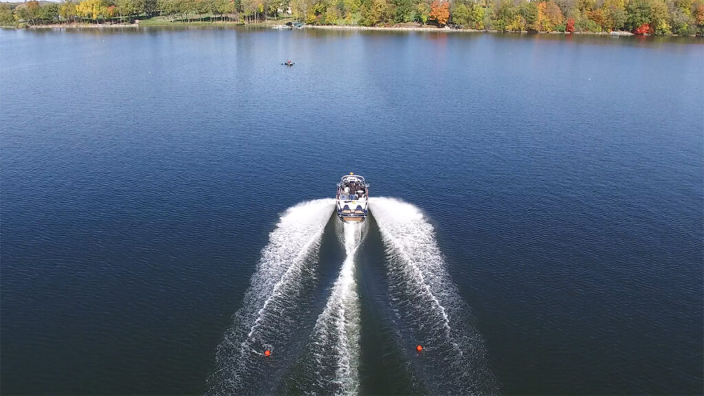 A wakeboat seen from above, with frothy white waves churning off the stern