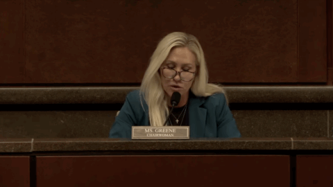 A woman with blonde hair, seated, speaks into a microphone. A name placard reads "Ms. Greene," and "Chairwoman."