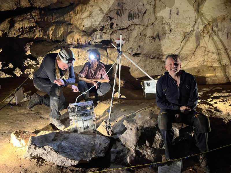 Three researchers sit in a darkened cave around monitoring equipment.