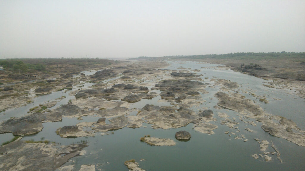 A shallow green-blue river with large brown-gray rocks.