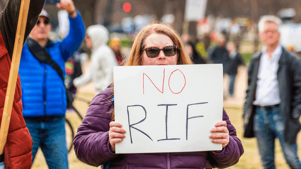 A woman at a protest holds up a sign that says "No RIF"