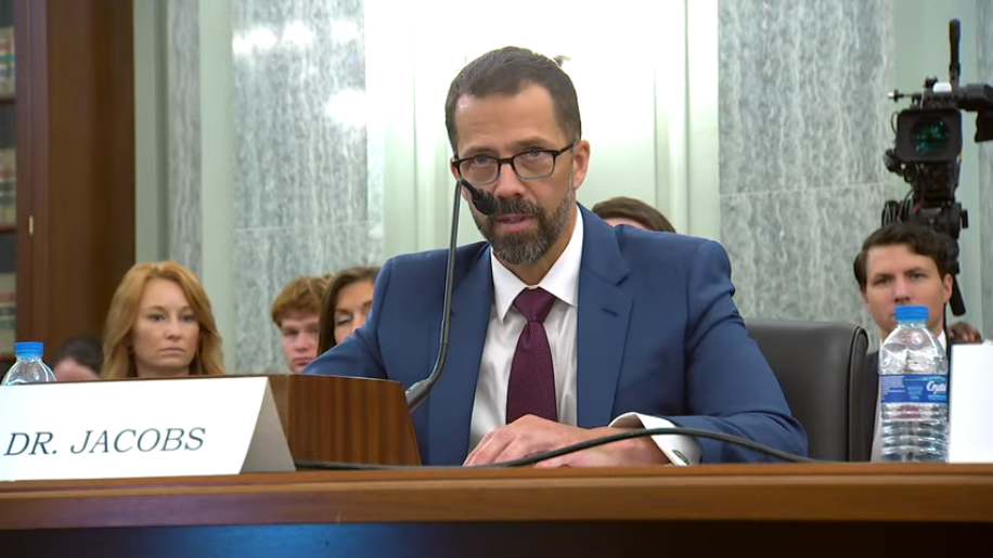 Neil Jacobs sits behind a microphone, speaking at his confirmation hearing.